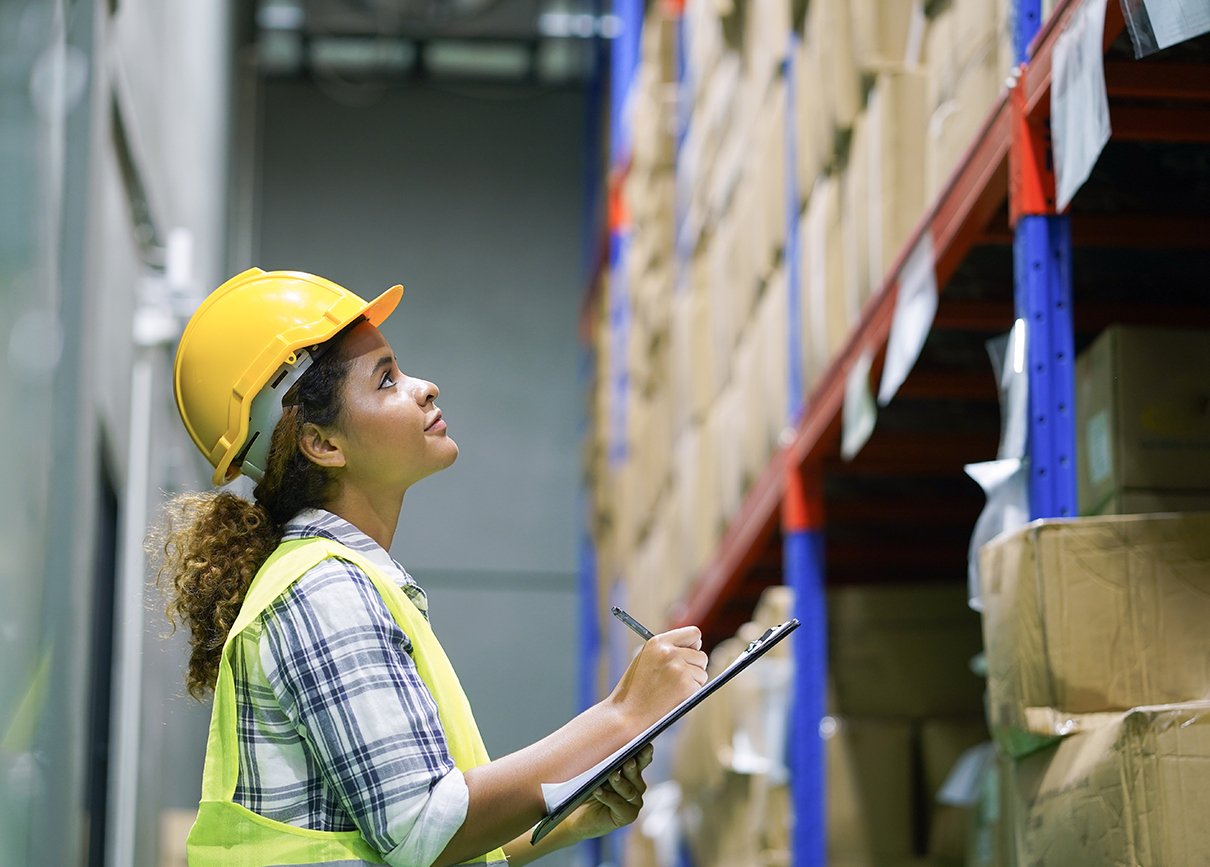 Supply chain worker inspecting stock with a checklist in a warehouse.