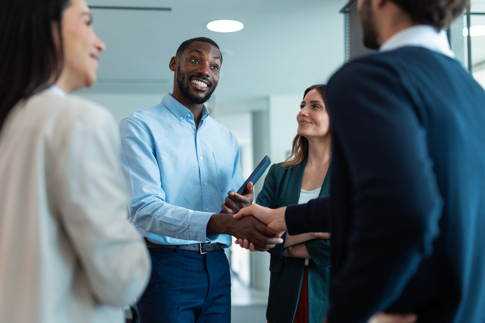 Man smiling while shaking hands with another person standing amongst a small group