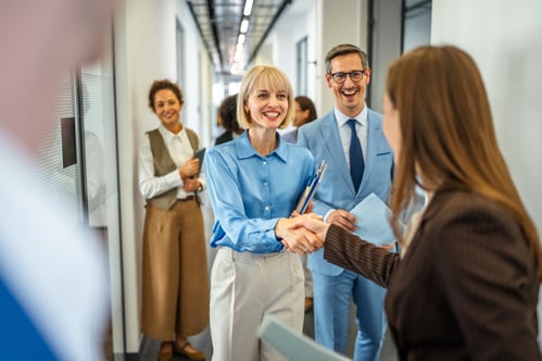 2 smiling women shaking hands among smiling peers