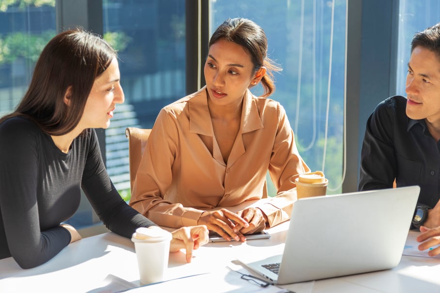 3 people sitting around a laptop collaborating in an office