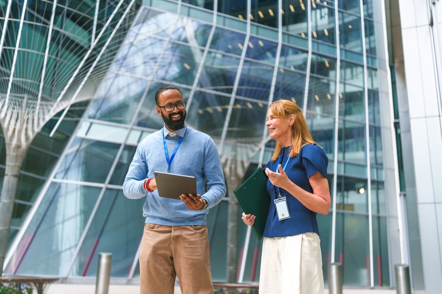 Happy colleagues discussing work and holding a tablet outside a modern building