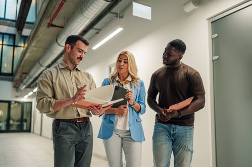 Three coworkers looking at paperwork together in the hallway