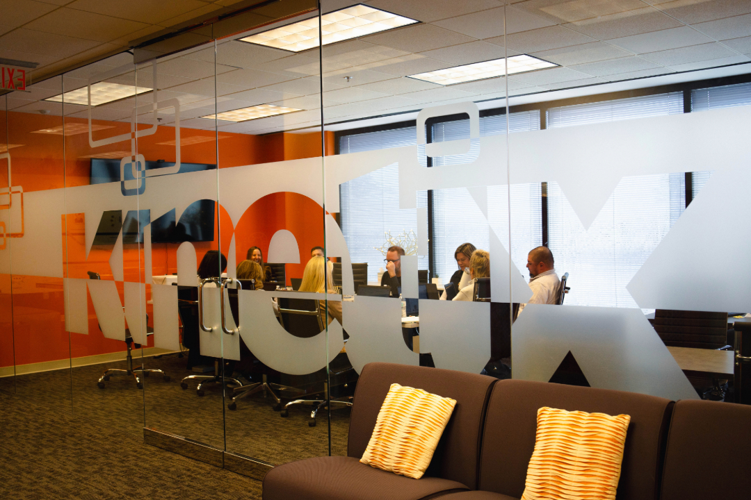 Coworkers in see-through meeting space with Kinetix logo
