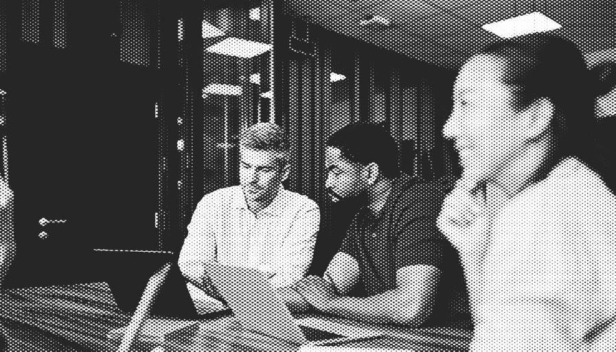 Focus on two colleagues sitting at a table looking at a laptop together 