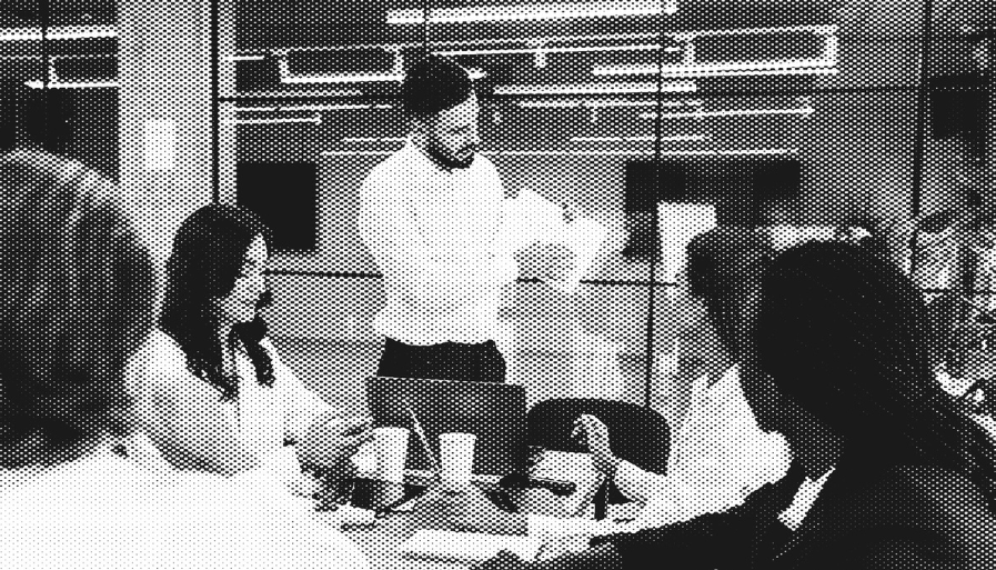 Person holding up paper with info while standing at head of table with colleagues