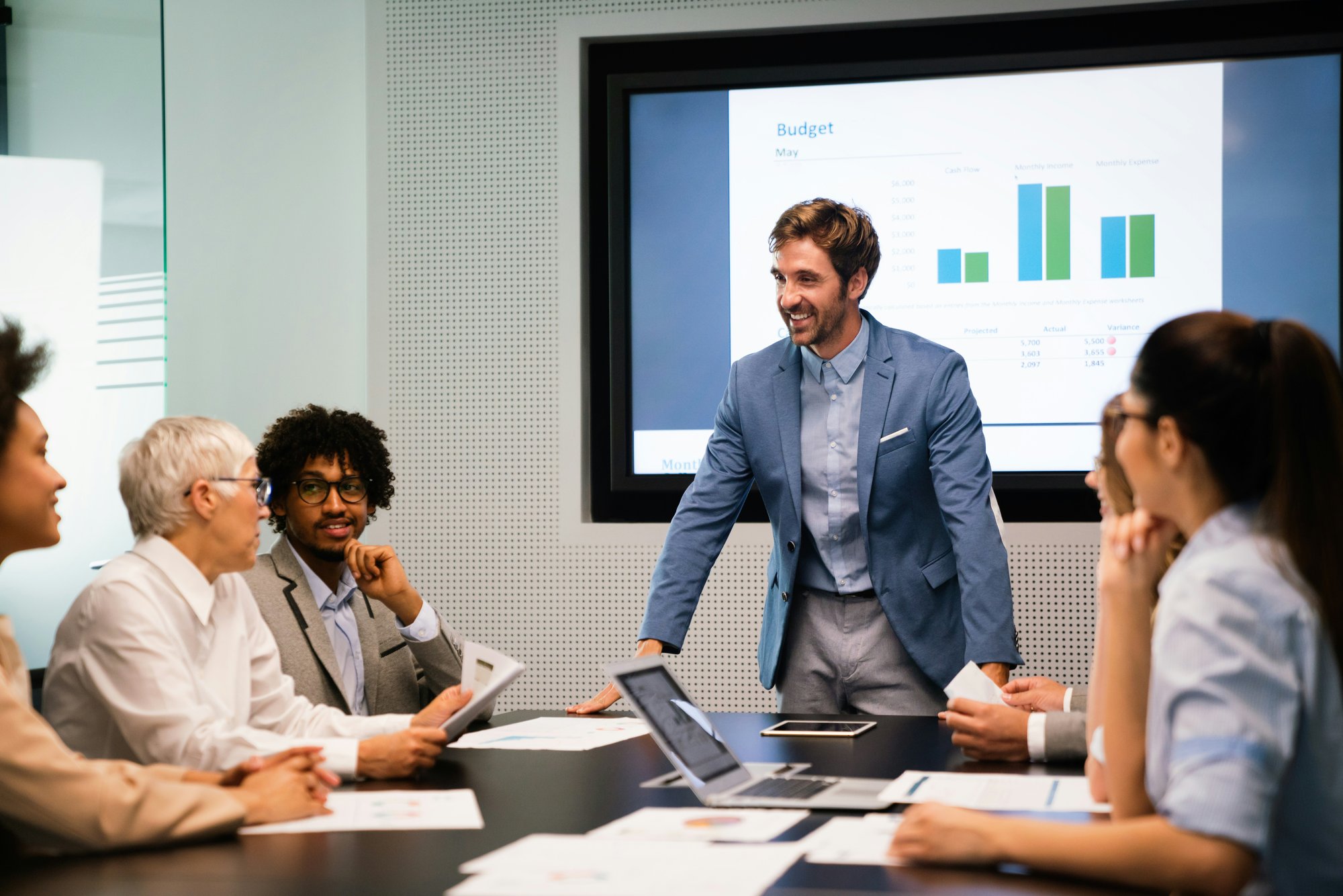 Group of people working together at a table with a slide showing stats on a screen behind
